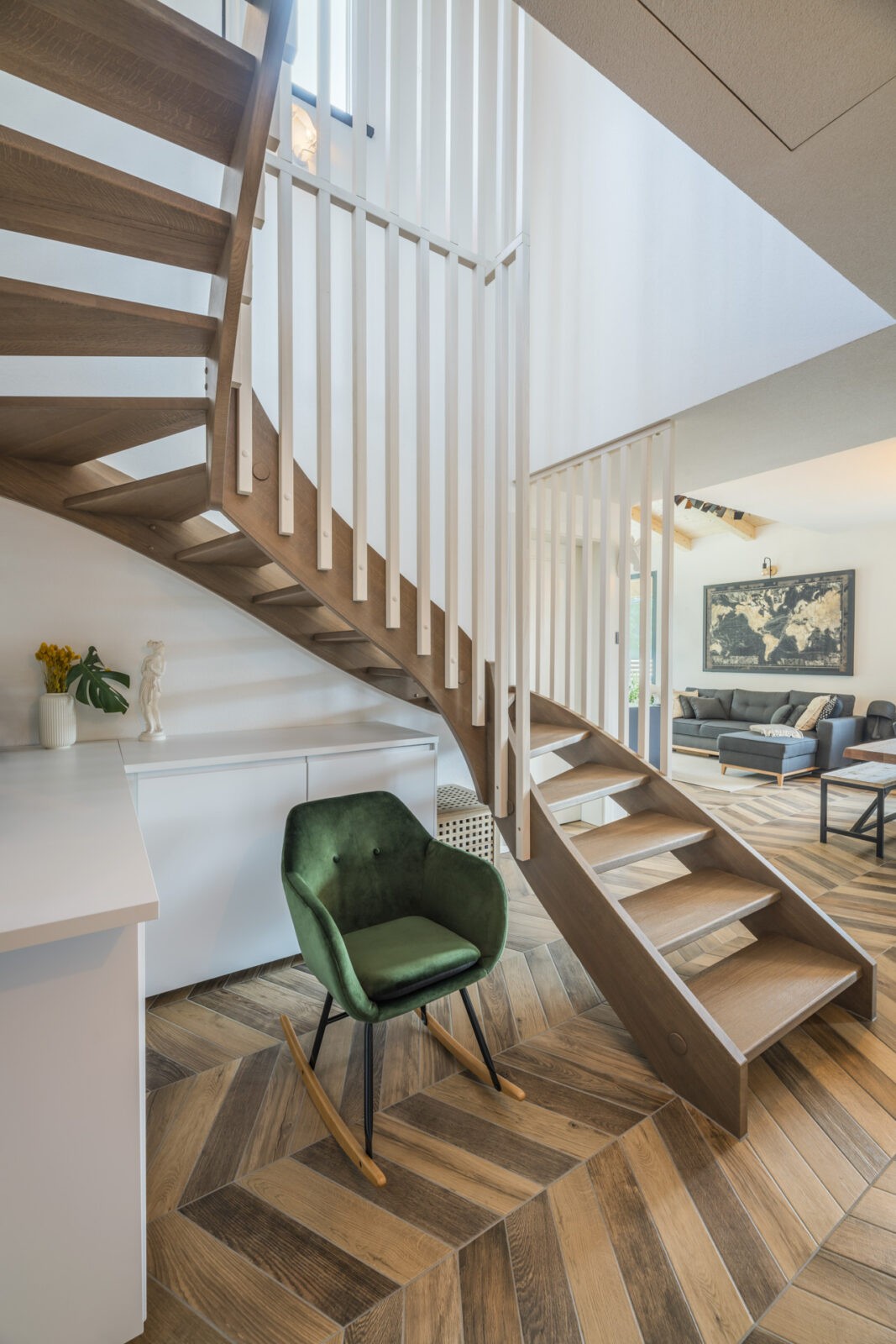 scala in legno all'interno di una lussuosa abitazione con parquet a lisca di pesce e sedia a dondolo in velluto verde